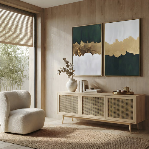 A styled interior scene with two framed abstract wall art prints hanging above a light wood sideboard. The room has warm wood walls and floor, a cream boucle armchair, a woven rug, and natural light coming from a window with blinds.