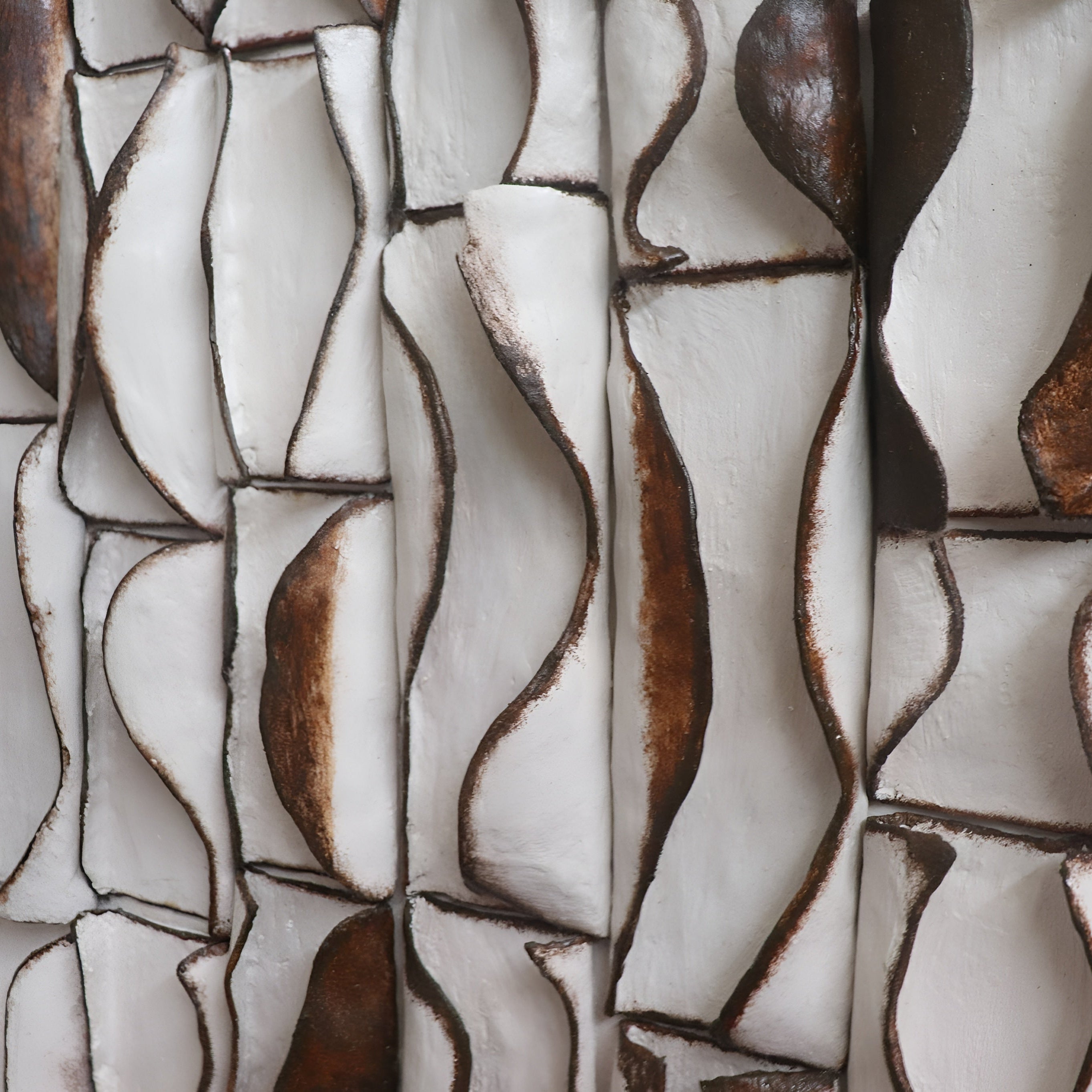 3D ceramic wall art sculpture with hand-formed hourglass column segments in warm cream and bronze glaze, mounted on a living room feature wall
